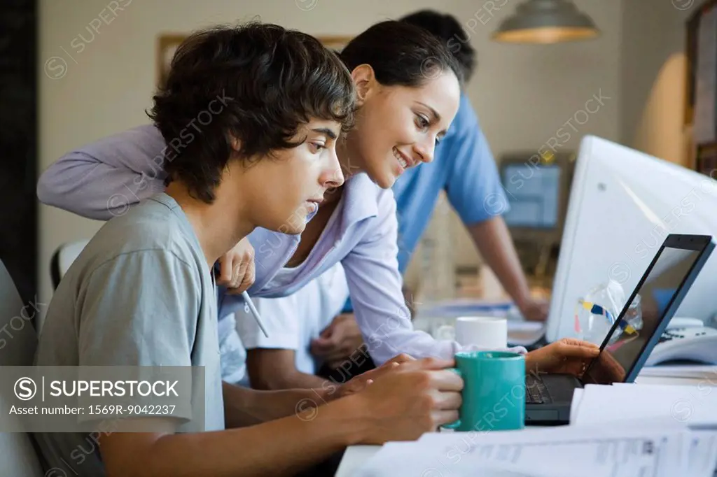 Male college student using laptop computer, female classmate looking over shoulder at laptop, smiling