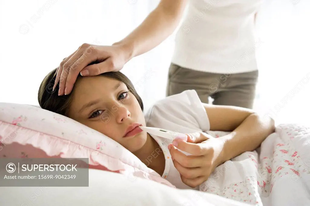 Girl checking temperature with thermometer, mother caressing forehead