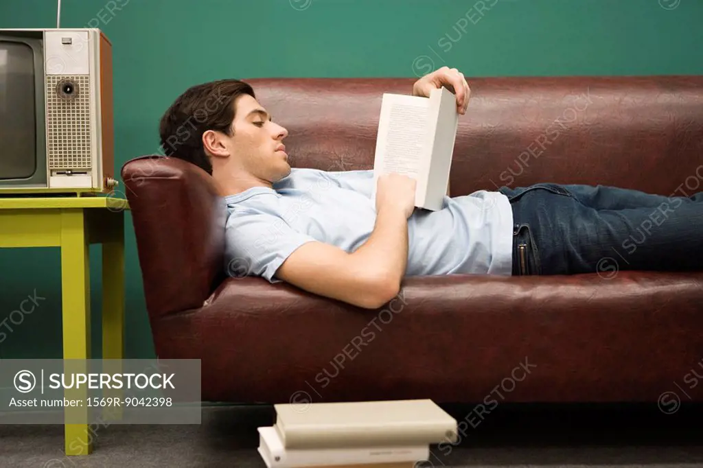 Young man relaxing on sofa with book