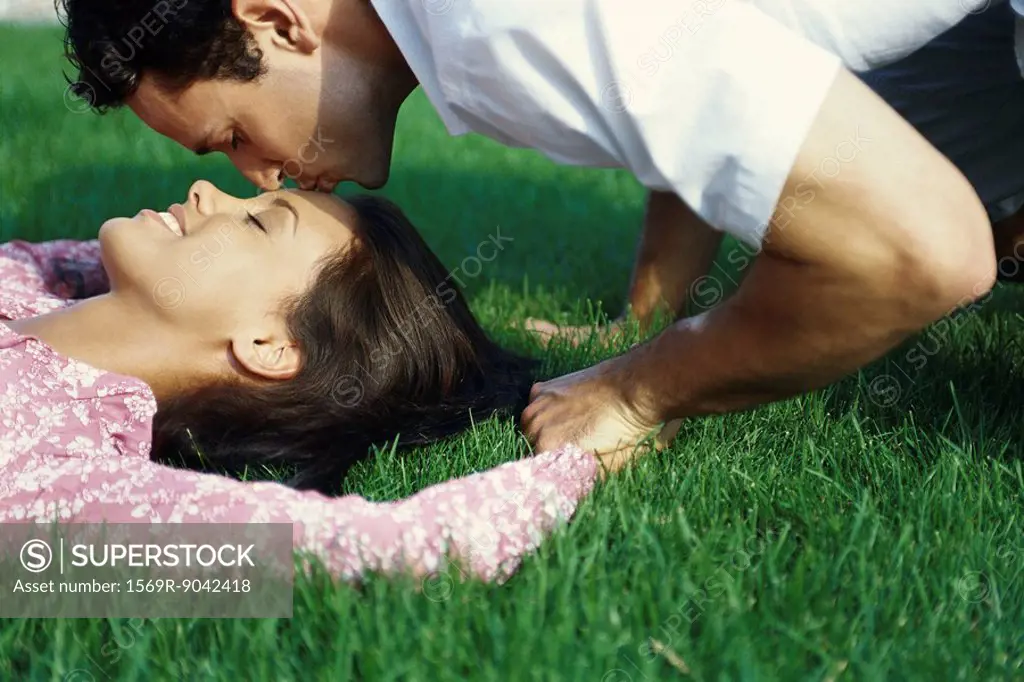 Young couple relaxing on grass, man kissing woman´s forehead