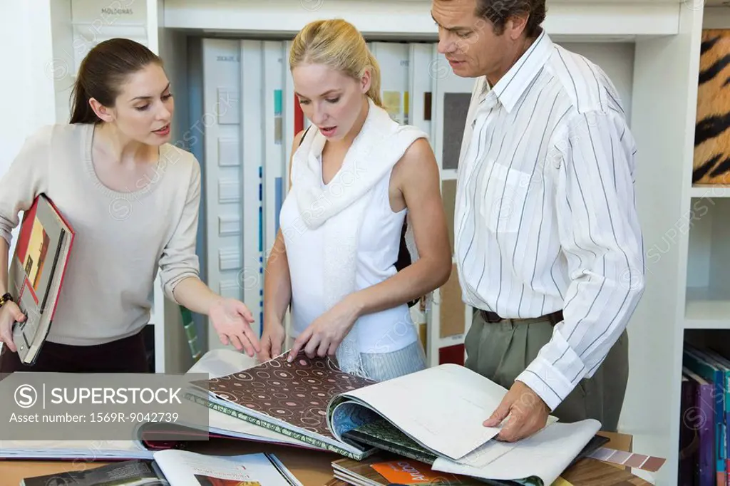 Woman assisting couple choosing wallpaper samples in store