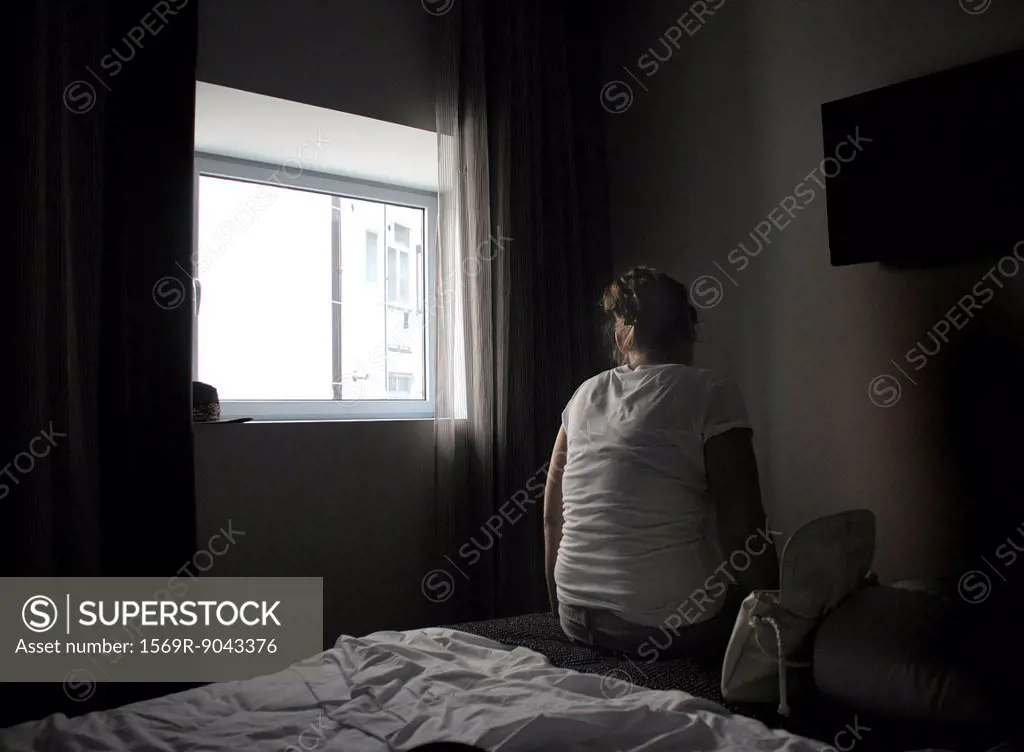 Female sitting alone on bed with back turned to camera