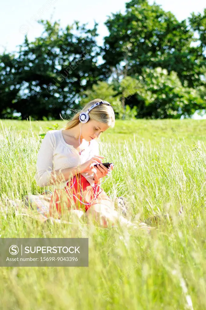 Young woman sitting in tall grass listening to headphones