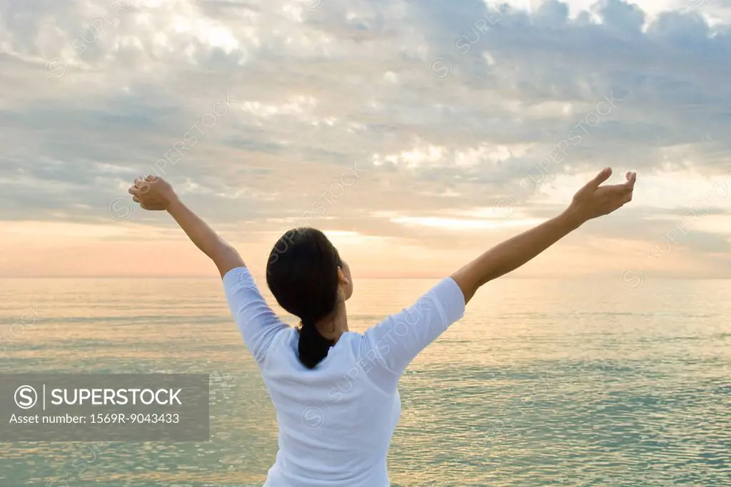 Woman watching sunset at the beach, arms raised in the air