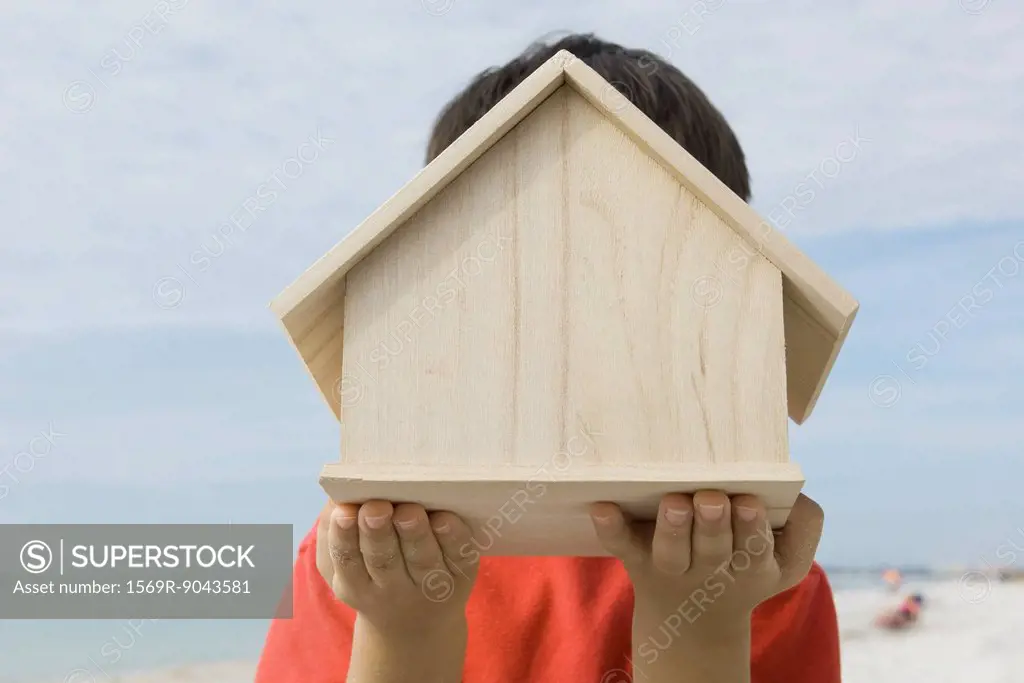 Boy holding wooden birdhouse in front of face