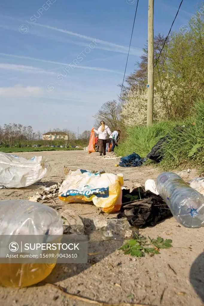 Trash dumped on dirt road, volunteers in background cleaning up