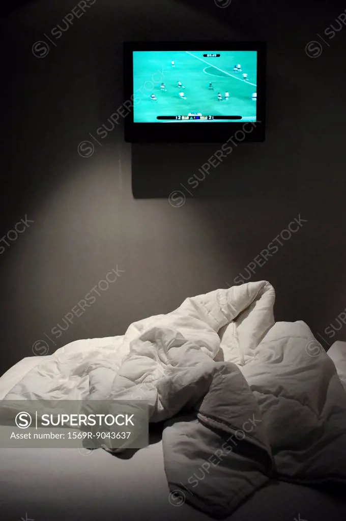 Sports match on flat screen TV mounted over bed
