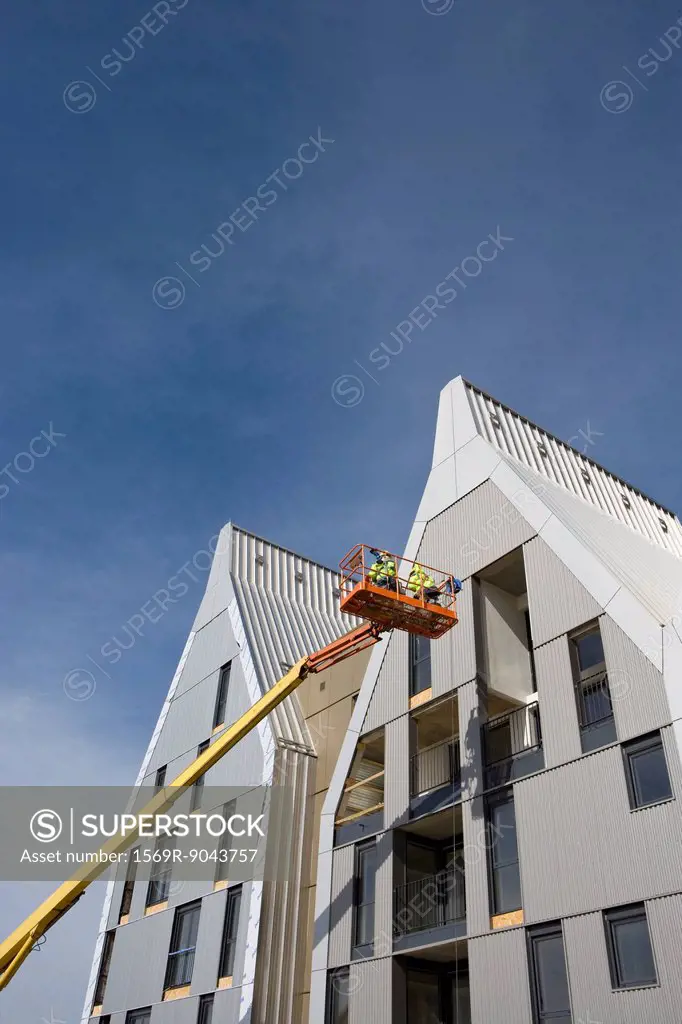 Construction workers in cherry picker bucket working on building exterior