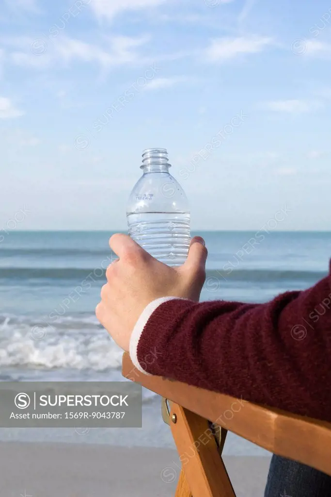 Person sitting relaxing at the beach, water bottle in hand