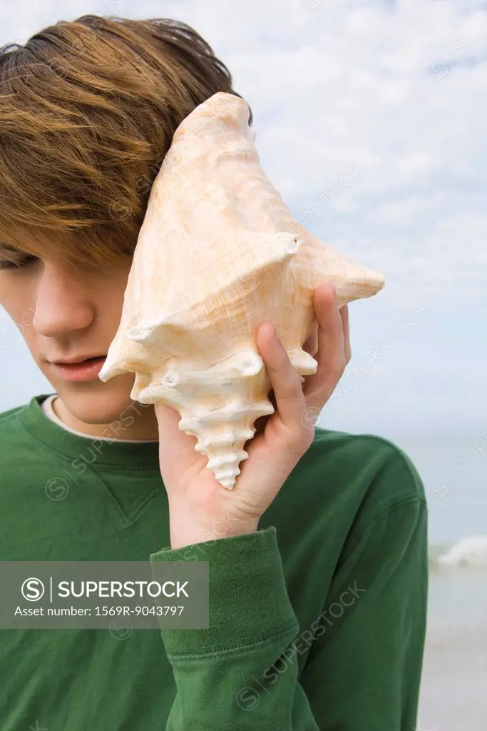 Young male listening to conch shell