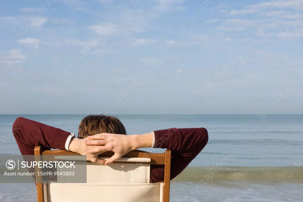 Person relaxing in chair on beach, rear view