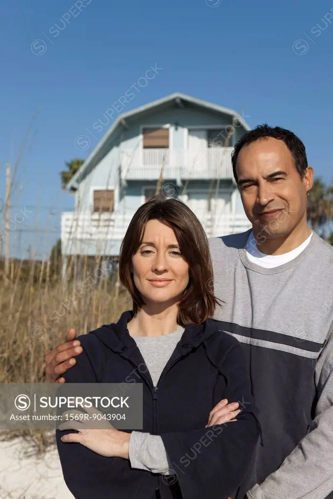 Mature couple standing in front of beach house, portrait