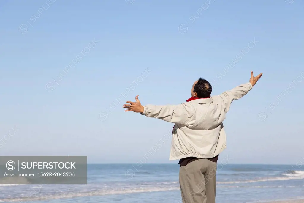 Man standing on beach looking at ocean with arms out