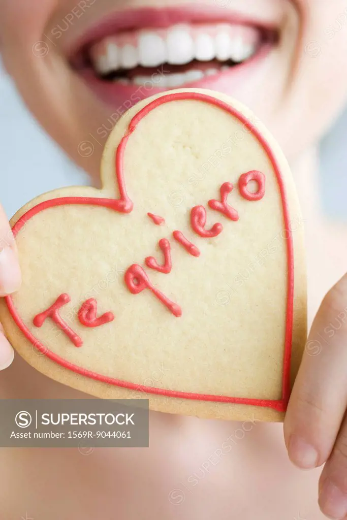 Woman holding up heart_shaped cookie, smiling, cropped