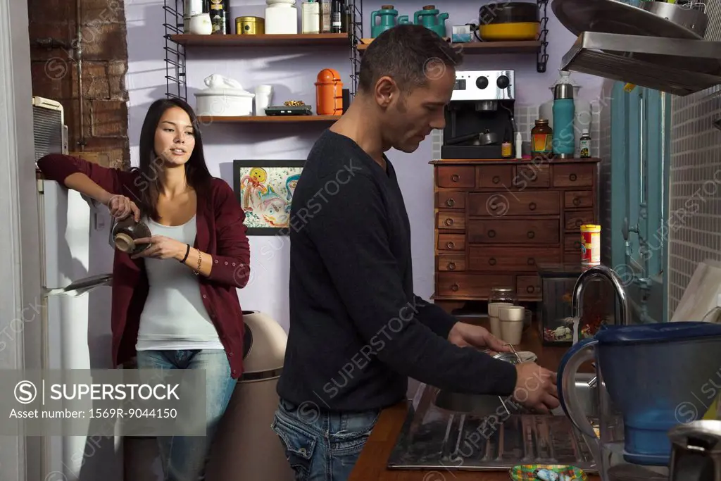 Couple in kitchen, husband doing dishes