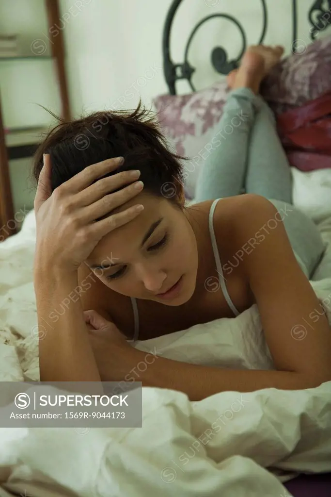 Young woman lying on bed looking sad, portrait