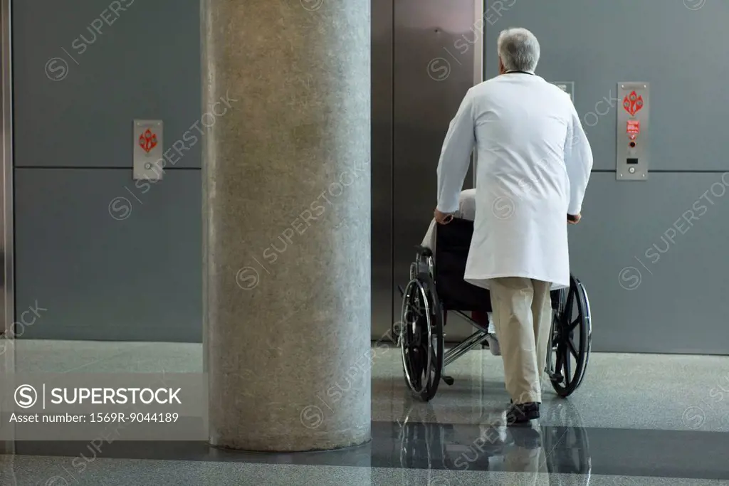 Doctor pushing patient in wheelchair toward elevator