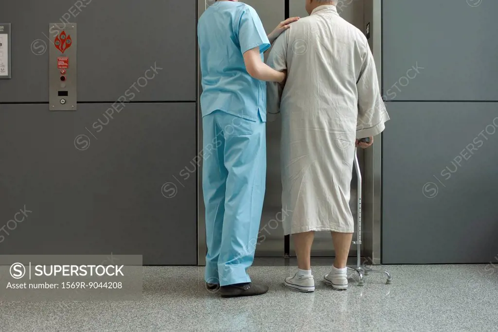 Nurse helping patient wait for elevator in hospital corridor