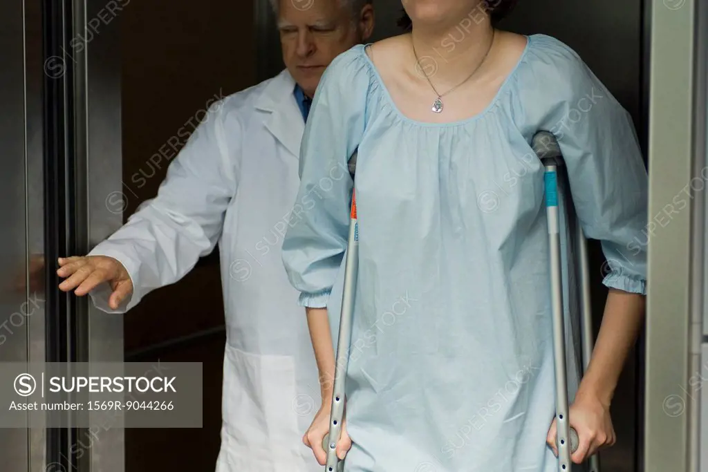Doctor holding elevator door for patient using crutches