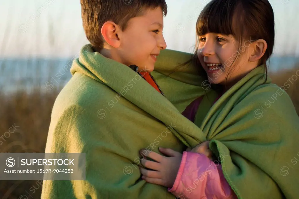 Children wrapped together in blanket outdoors, portrait