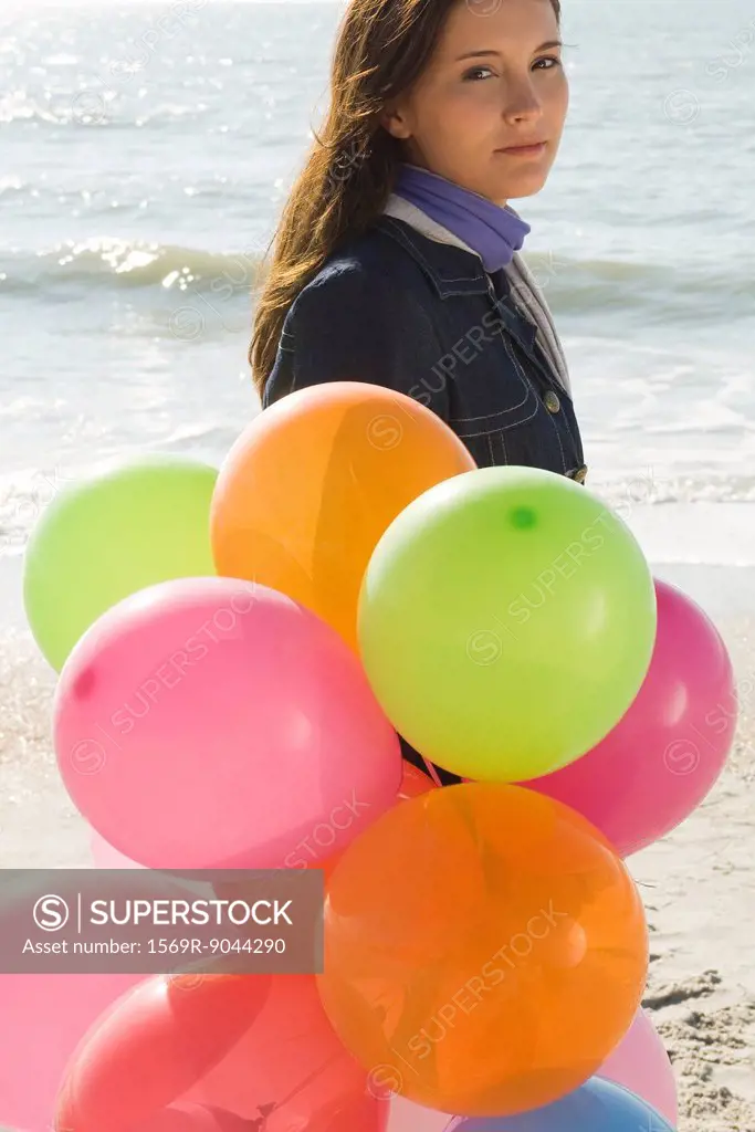 Preteen girl with bunch of balloons walking on beach