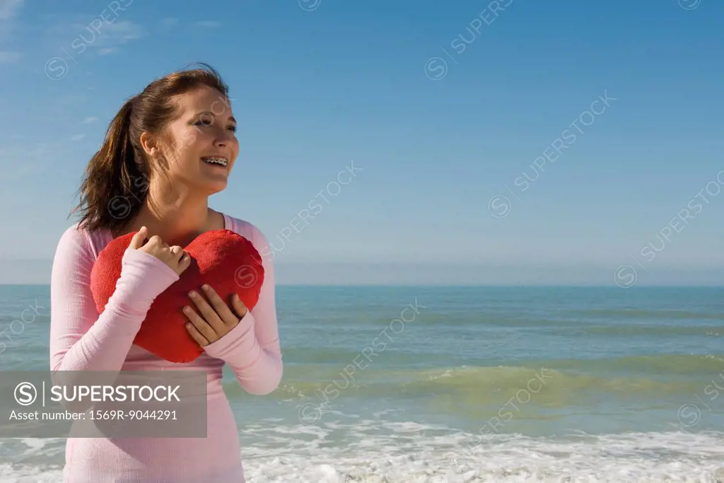 Preteen girl at beach holding stuffed heart_shaped toy contemplating love
