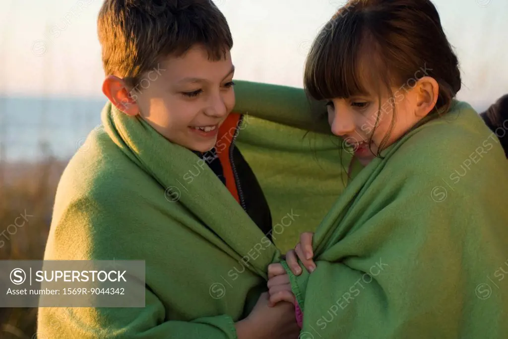 Children wrapped together in blanket outdoors, portrait