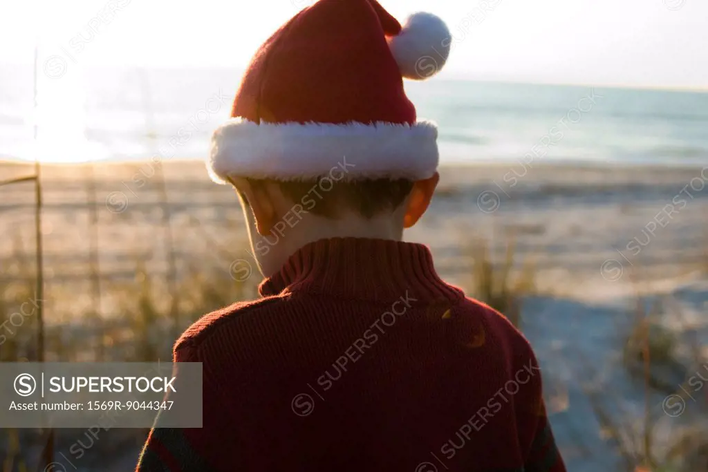 Boy exploring outdoors wearing Santa hat, beach in background