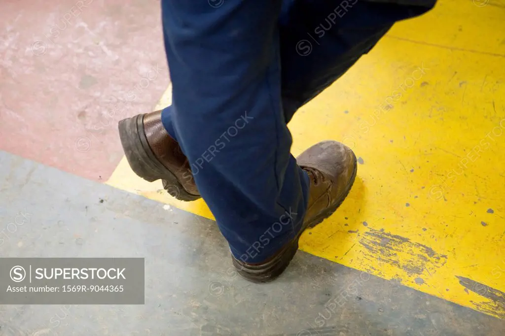 Factory worker wearing protective boots, standing with legs crossed at ankle, cropped