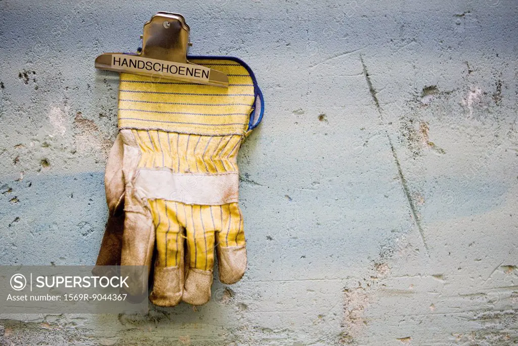 Protective work gloves held up by a binder clip on wall