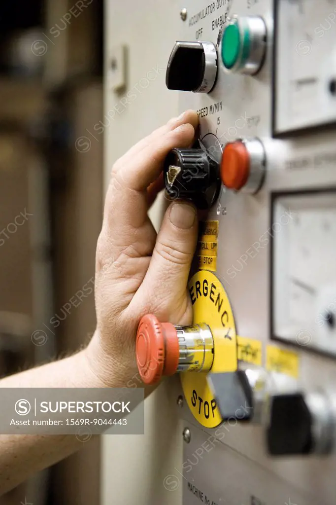 Worker adjusting speed knob on shearing machine control panel in carpet tile factory