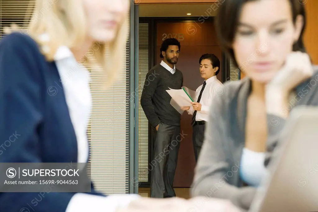 Executives discussing document in office doorway