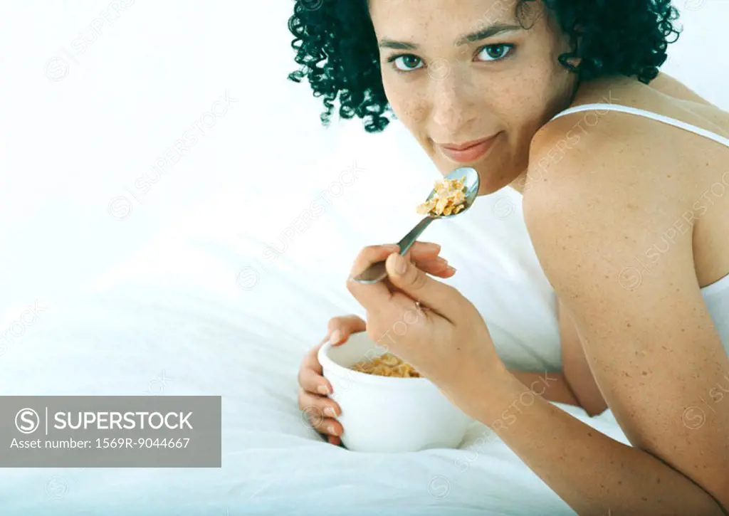Woman lying on stomach in bed, eating cereal