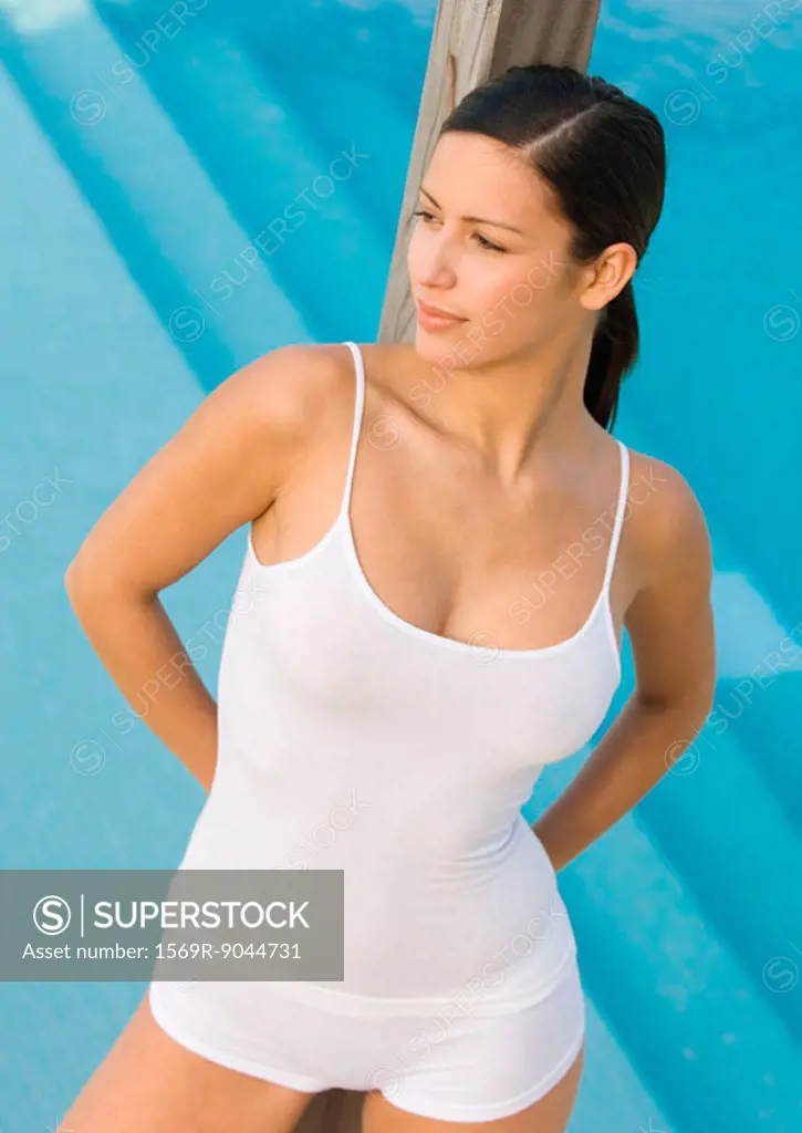 Woman leaning against wooden pole, swimming pool in background