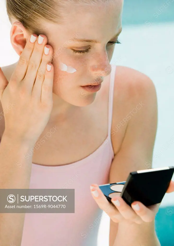 Woman applying sunscreen, looking into compact mirror