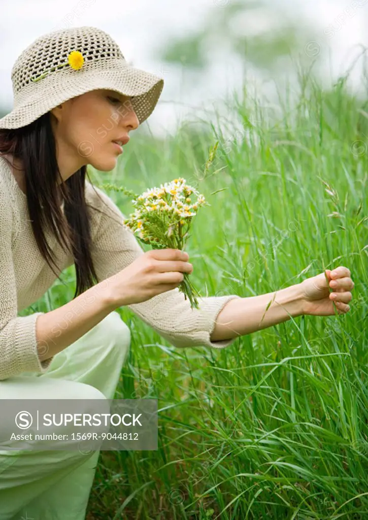 Woman crouching in long grass, holding bunch of flowers