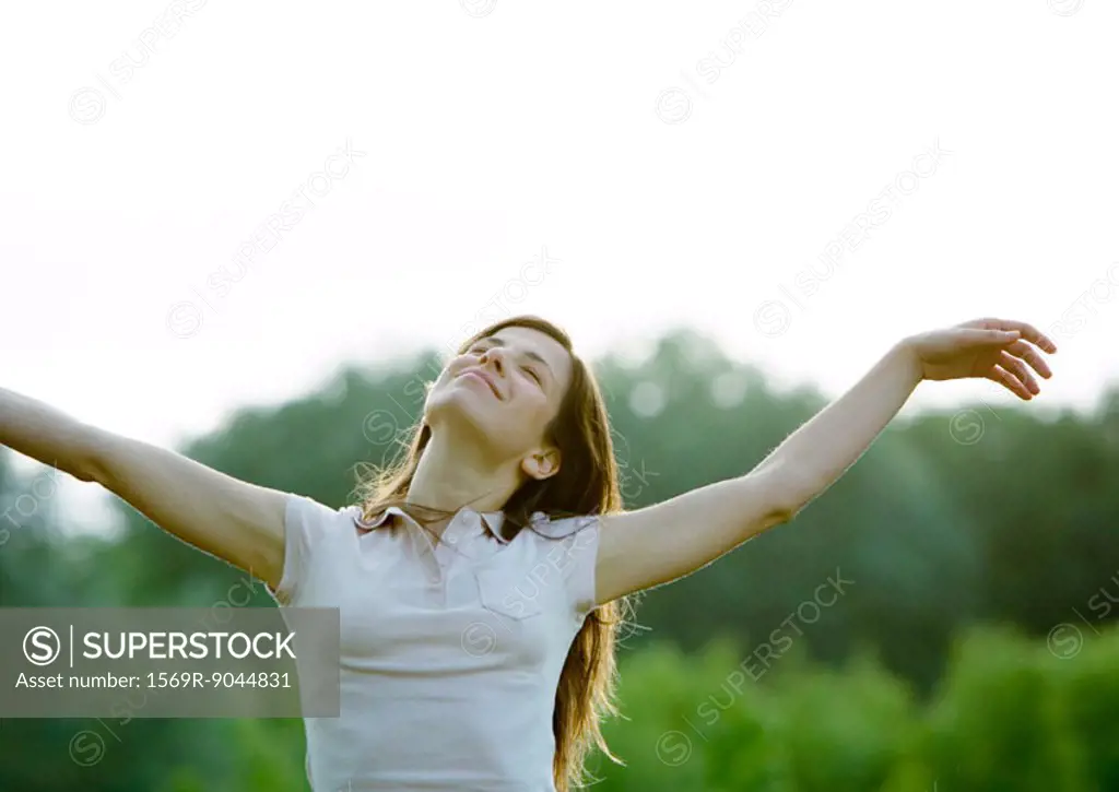 Woman standing outdoors with eyes closed and arms up