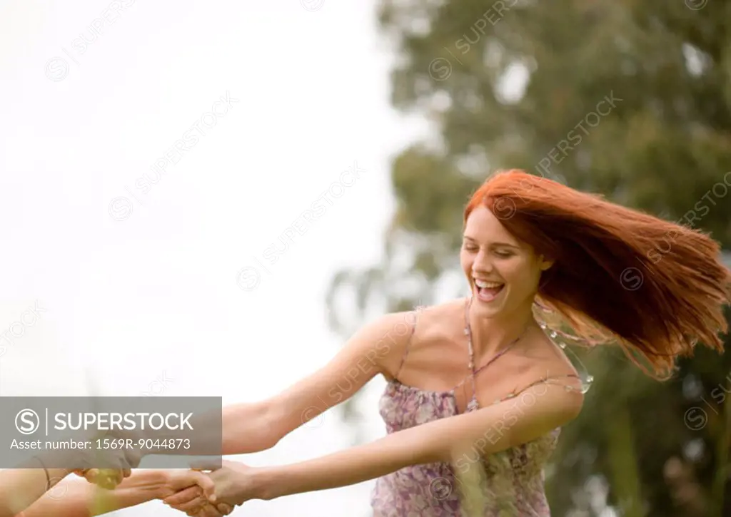 Young woman spinning around with friend outdoors