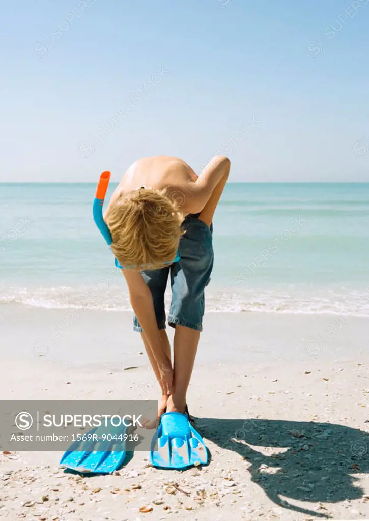 Boy wearing snorkel, putting on flippers