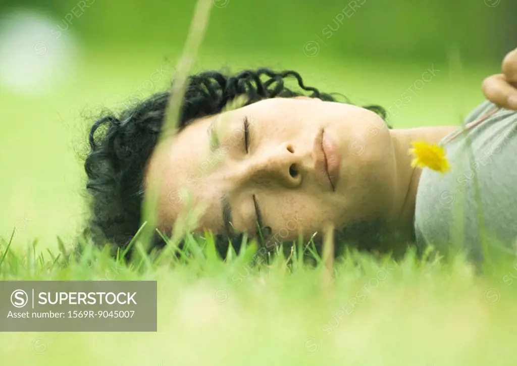 Woman lying on grass holding dandelion