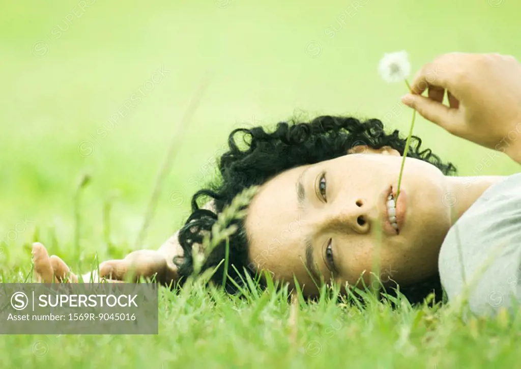 Woman lying on grass with dandelion in mouth