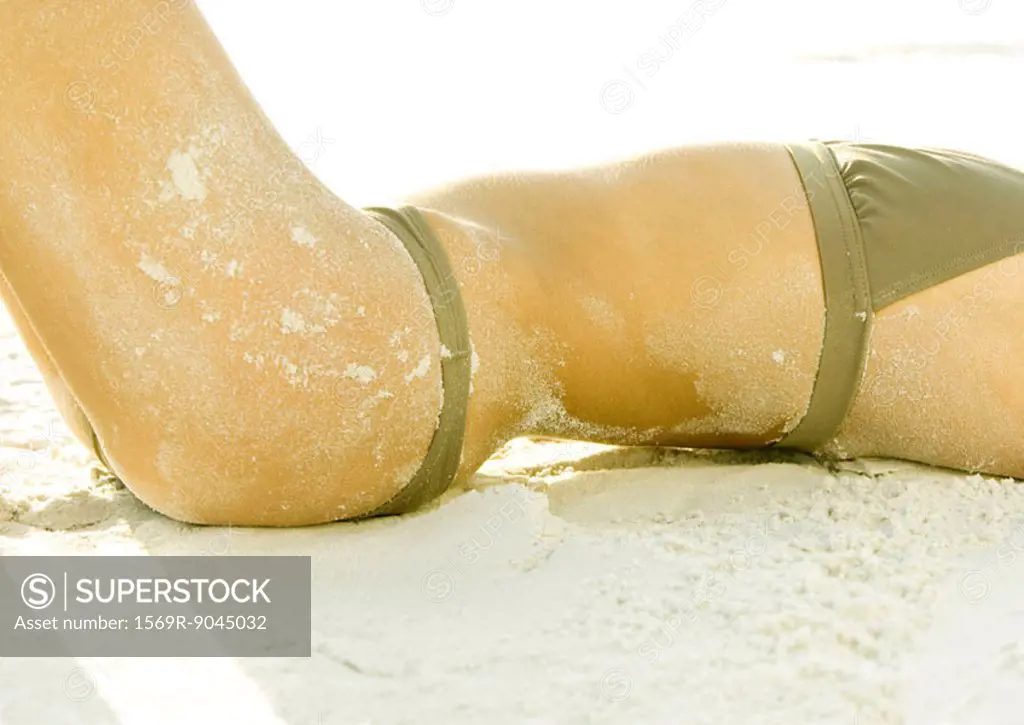 Woman lying on sand, mid-section
