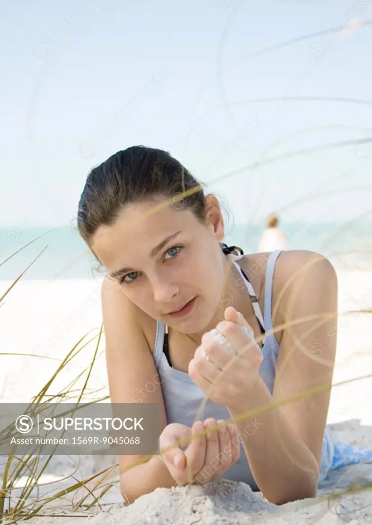 Girl lying on beach, letting sand run through hands
