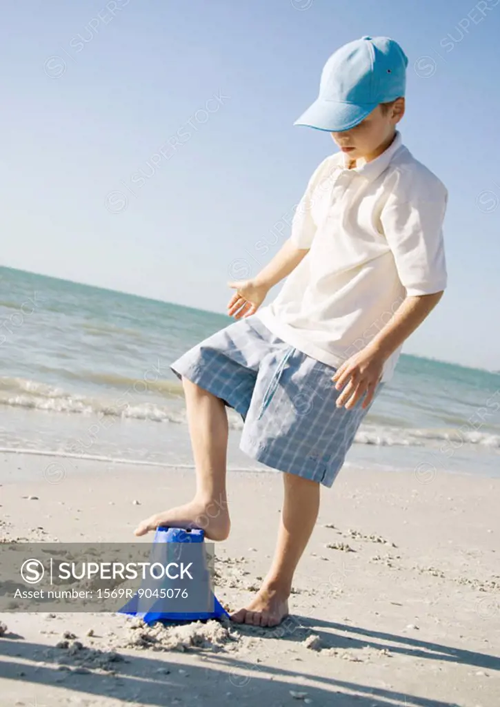 Boy stepping on sand bucket on beach