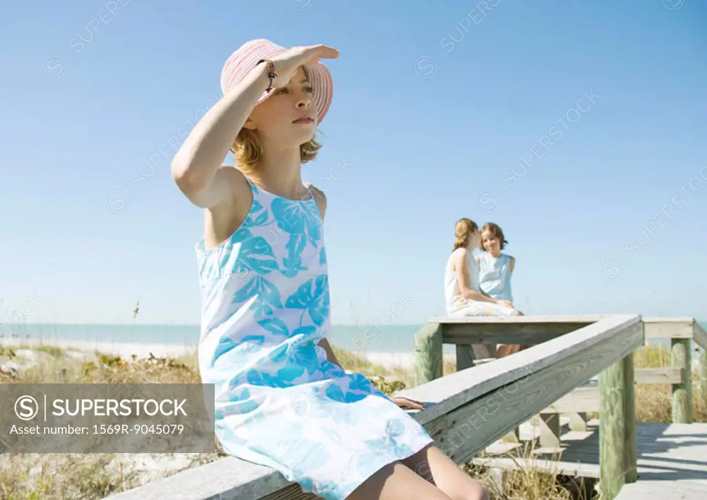 Girl sitting on railing of beach walkway, shading eyes