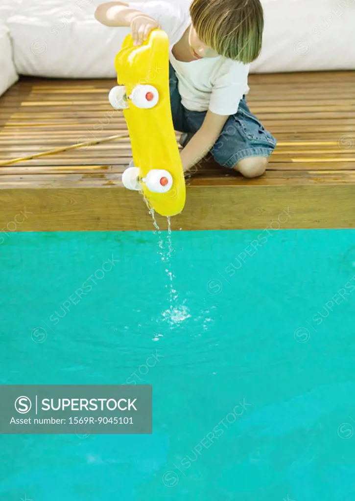 Boy holding dripping skateboard over edge of pool