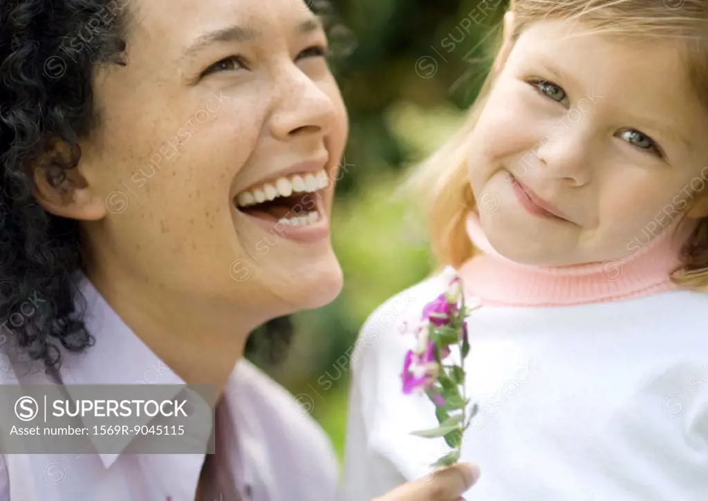 Woman laughing and holding flower, next to little girl