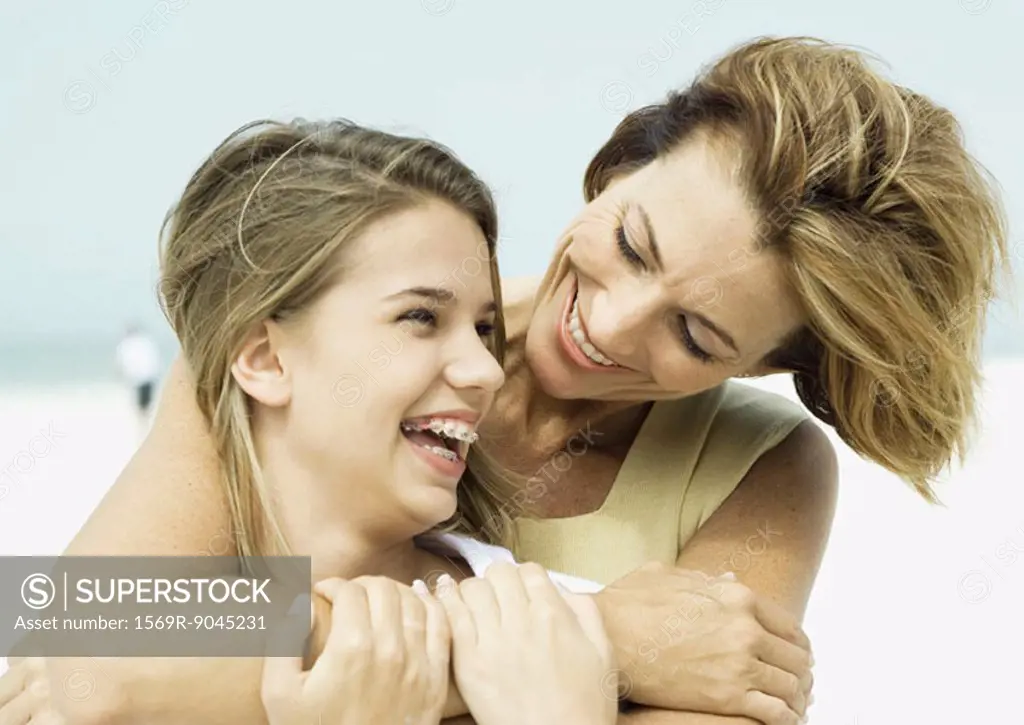Mother with arms around teenage daughter, smiling over her shoulder