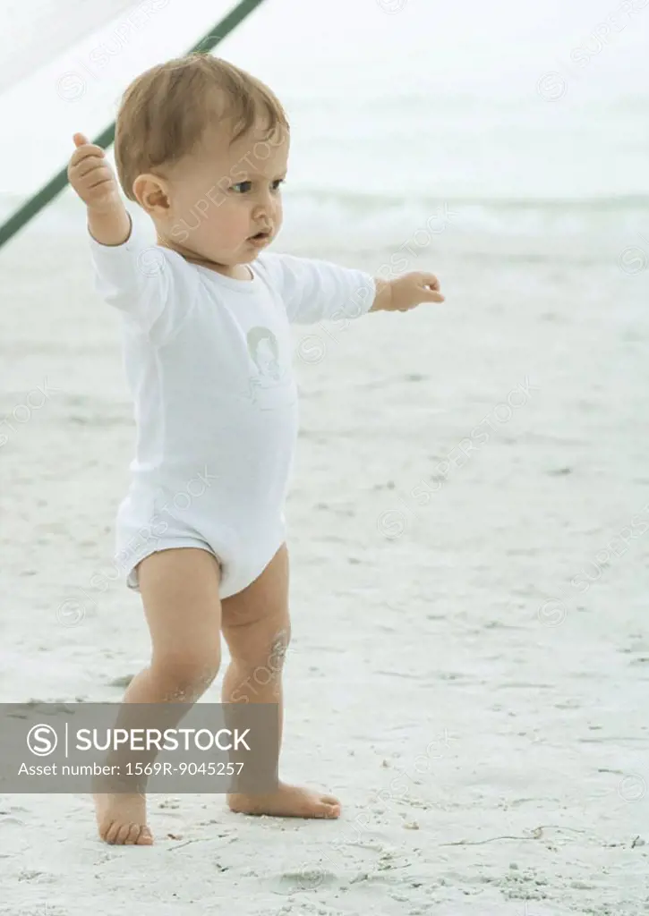 Baby walking on beach with arms outstretched