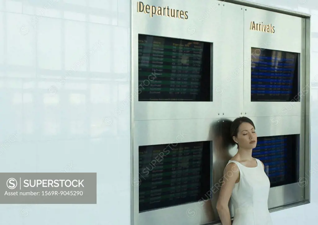 Woman leaning against arrival and departure boards with eyes closed